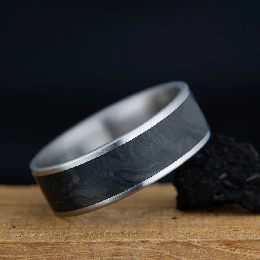 Silver ring with black inlay on a wooden surface with a dark background